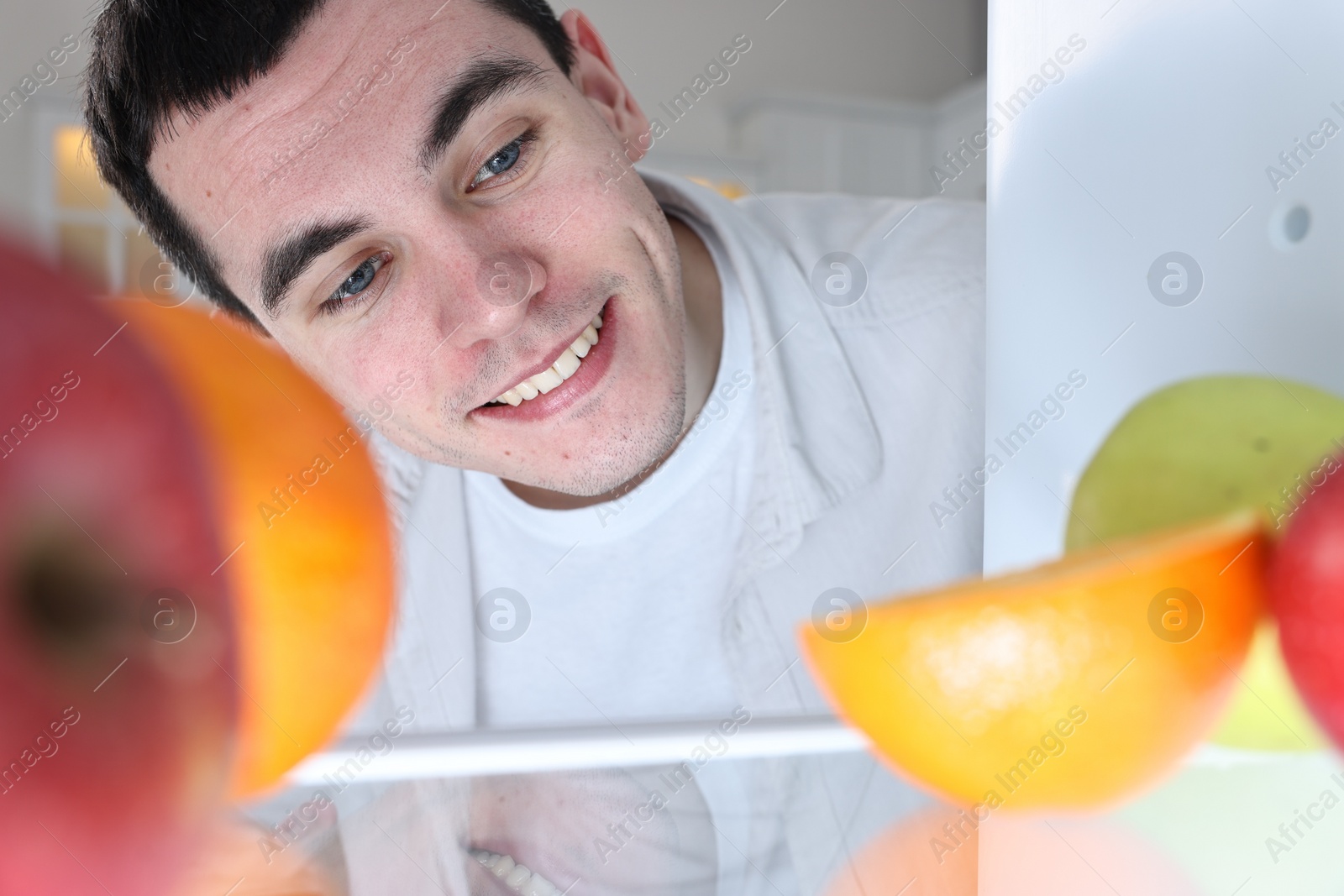 Photo of Happy man near refrigerator in kitchen, view from inside