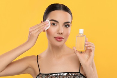 Beautiful woman removing makeup with cotton pad on orange background