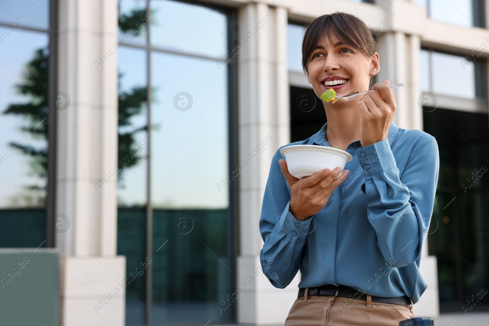 Photo of Happy businesswoman with plastic bowl of salad having lunch outdoors