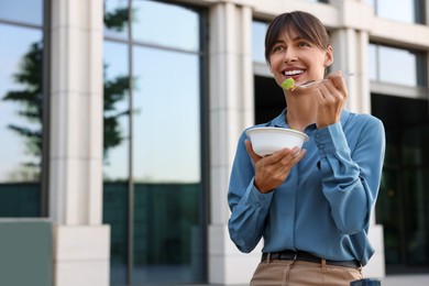 Photo of Happy businesswoman with plastic bowl of salad having lunch outdoors