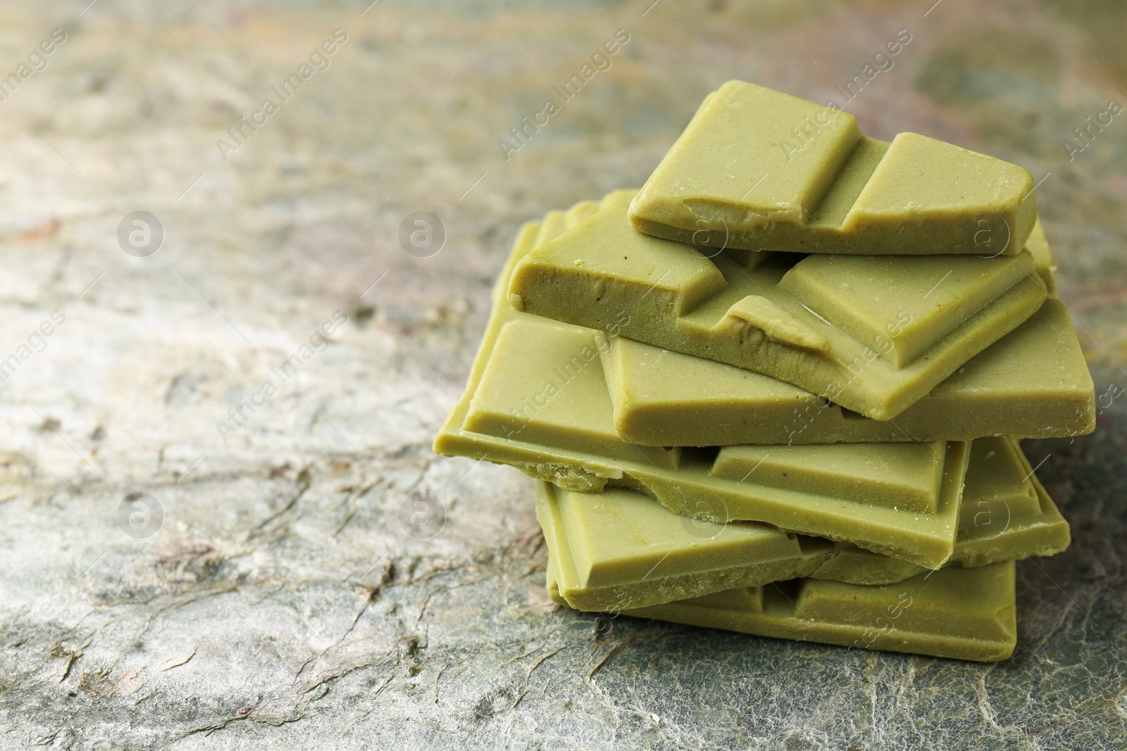 Photo of Stacked pieces of tasty matcha chocolate on textured table, closeup. Space for text