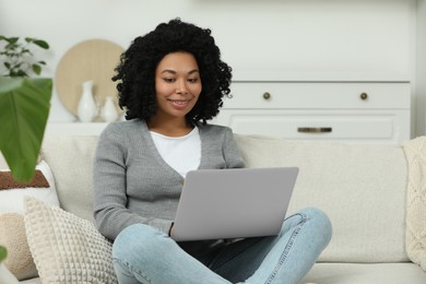 Happy young woman using laptop on sofa indoors