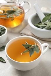 Photo of Cup of sage tea with green leaves on white table