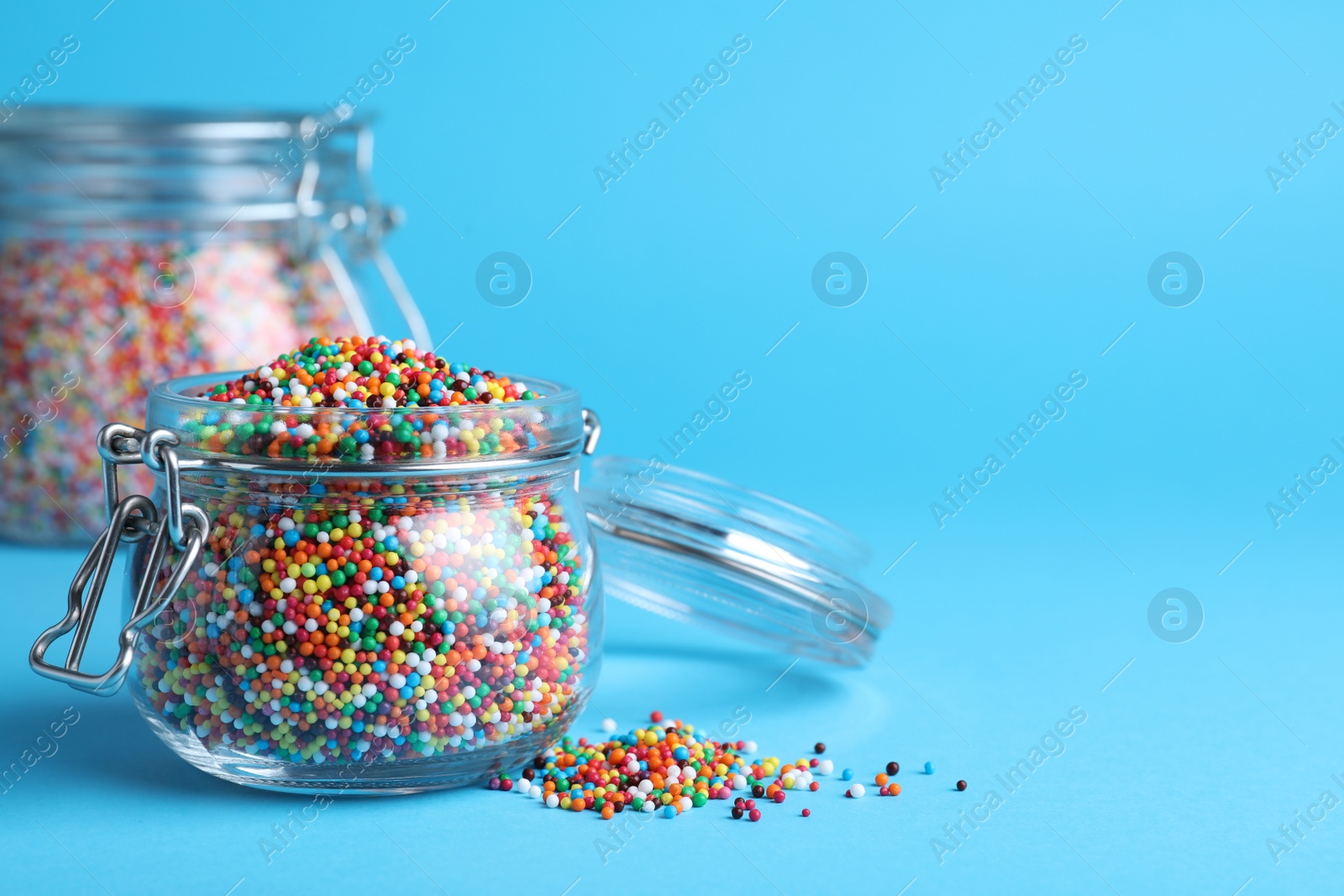 Photo of Colorful sprinkles and jar on light blue background, space for text. Confectionery decor