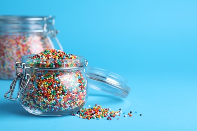 Photo of Colorful sprinkles and jar on light blue background, space for text. Confectionery decor