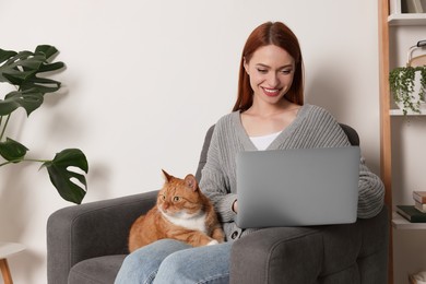 Happy woman with cat working in armchair at home