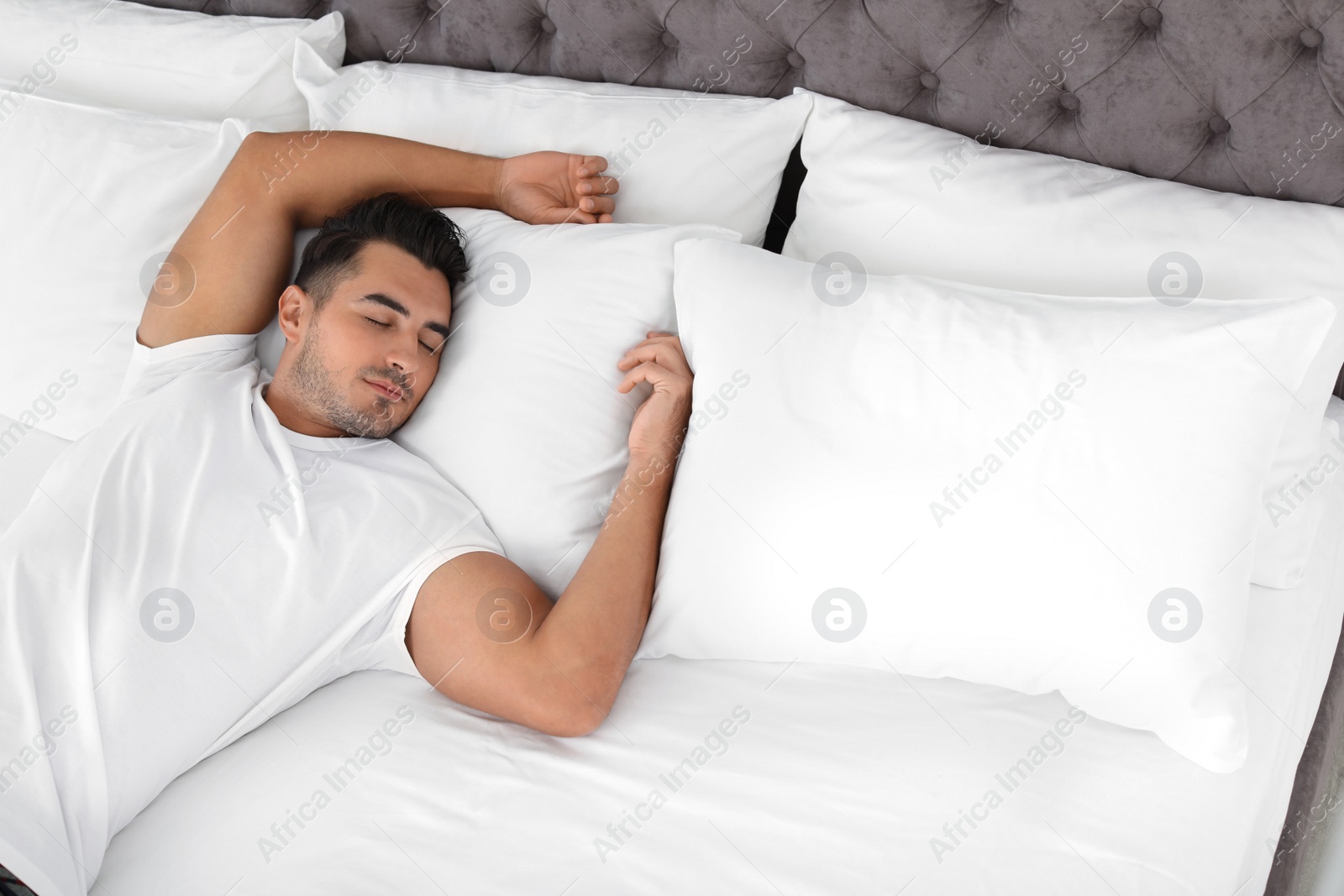 Photo of Young man sleeping on bed with soft pillows at home