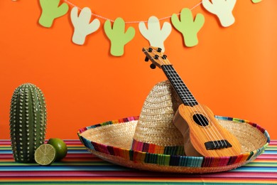 Composition with Mexican sombrero hat and ukulele on color table, closeup