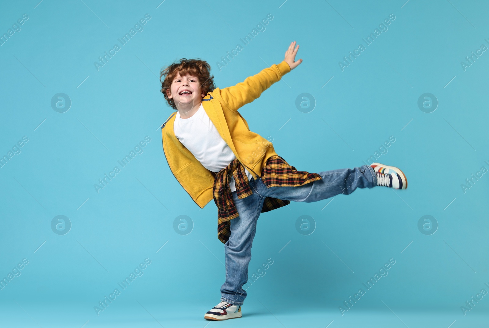 Photo of Happy little boy dancing on light blue background. Space for text