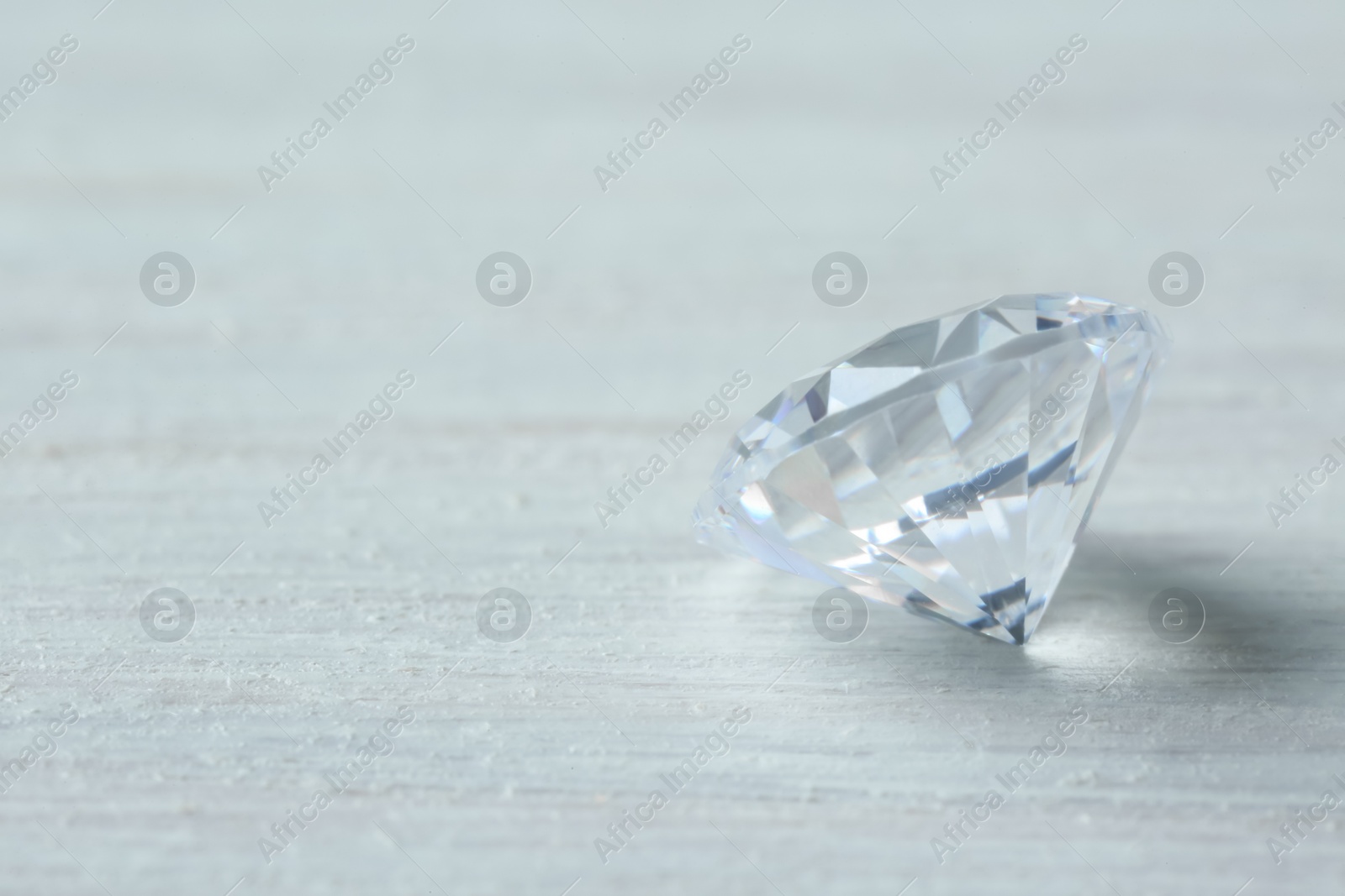 Photo of Beautiful shiny diamond on light wooden table, space for text