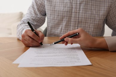 Photo of Businesspeople signing contract at wooden table indoors, closeup of hands