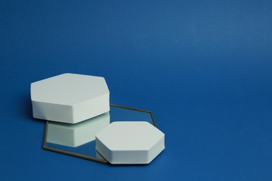Photo of Product photography props. Hexagonal shaped podiums and mirror on blue background, space for text