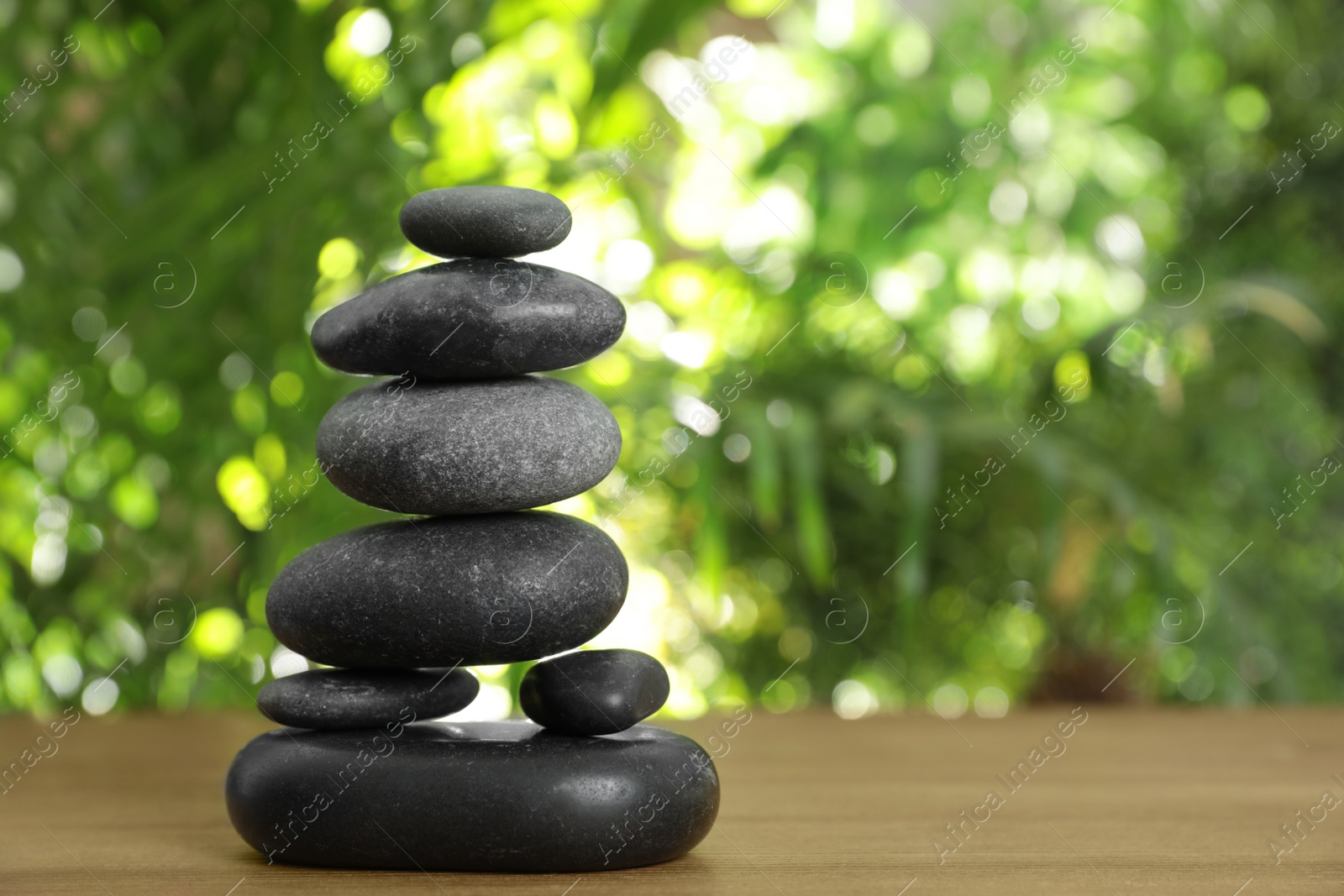 Photo of Table with stack of stones and blurred green leaves on background, space for text. Zen concept