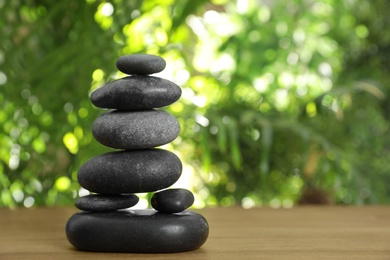 Photo of Table with stack of stones and blurred green leaves on background, space for text. Zen concept