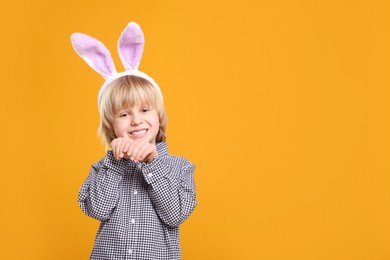 Photo of Happy boy wearing bunny ears headband on orange background, space for text. Easter celebration