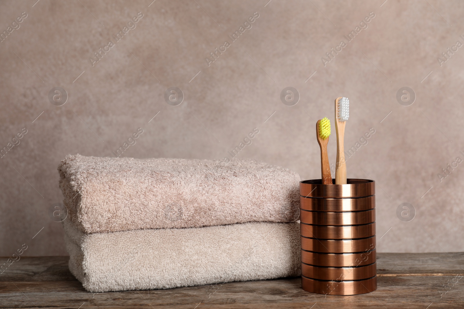 Photo of Holder with bamboo toothbrushes and towels on table against grey background