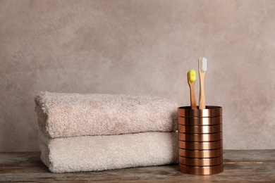 Holder with bamboo toothbrushes and towels on table against grey background