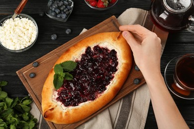 Woman eating delicious sweet cottage cheese pastry with cherry jam at wooden table, top view
