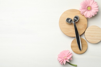 Metal face roller and flowers on white wooden background, flat lay. Space for text