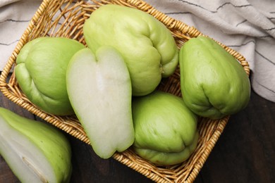 Cut and whole chayote in wicker basket on wooden table, top view