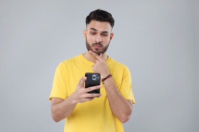 Handsome young man using smartphone on grey background