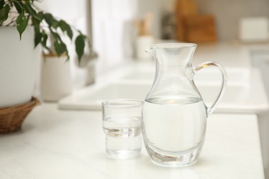 Jug and glass with clear water on white table in kitchen