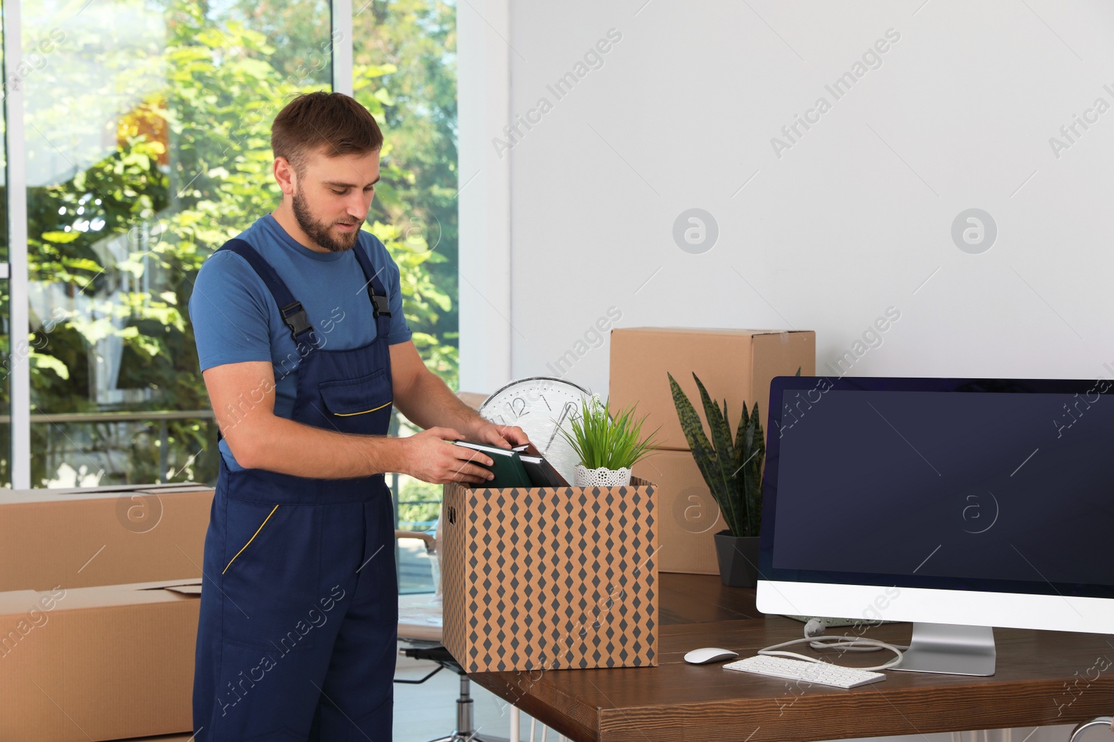 Photo of Young worker packing stuff into cardboard box at office. Moving service