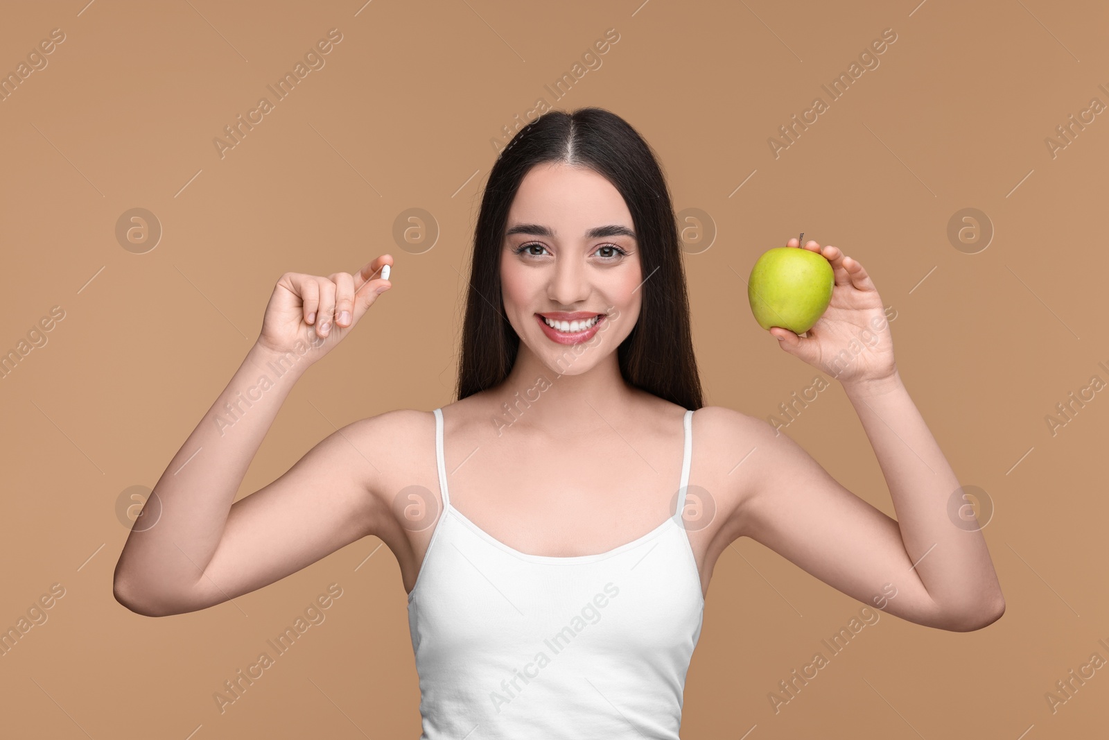 Photo of Beautiful young woman with vitamin pill and apple on beige background