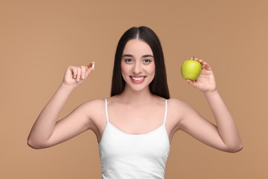 Beautiful young woman with vitamin pill and apple on beige background