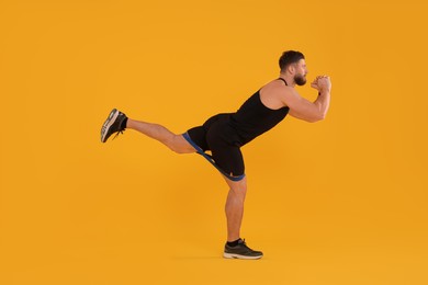 Young man exercising with elastic resistance band on orange background