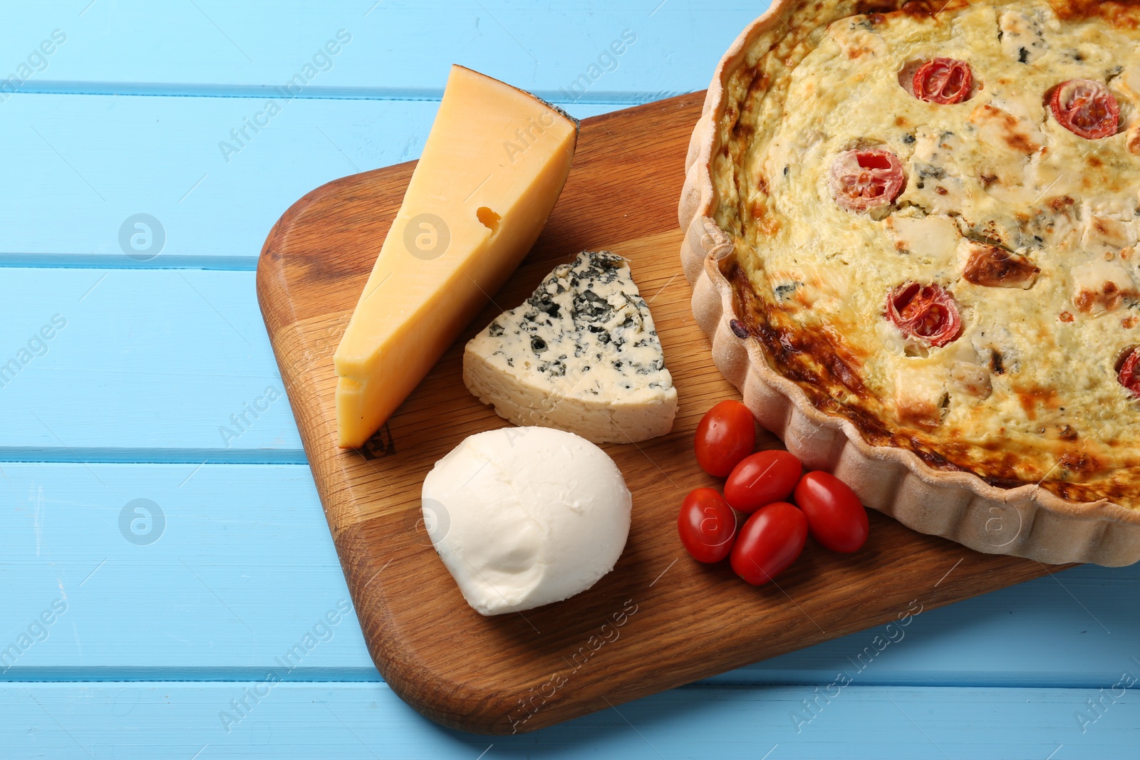 Photo of Delicious homemade cheese quiche and ingredients on light blue wooden table