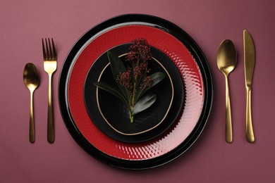 Stylish table setting with cutlery and floral decor on pink background, flat lay