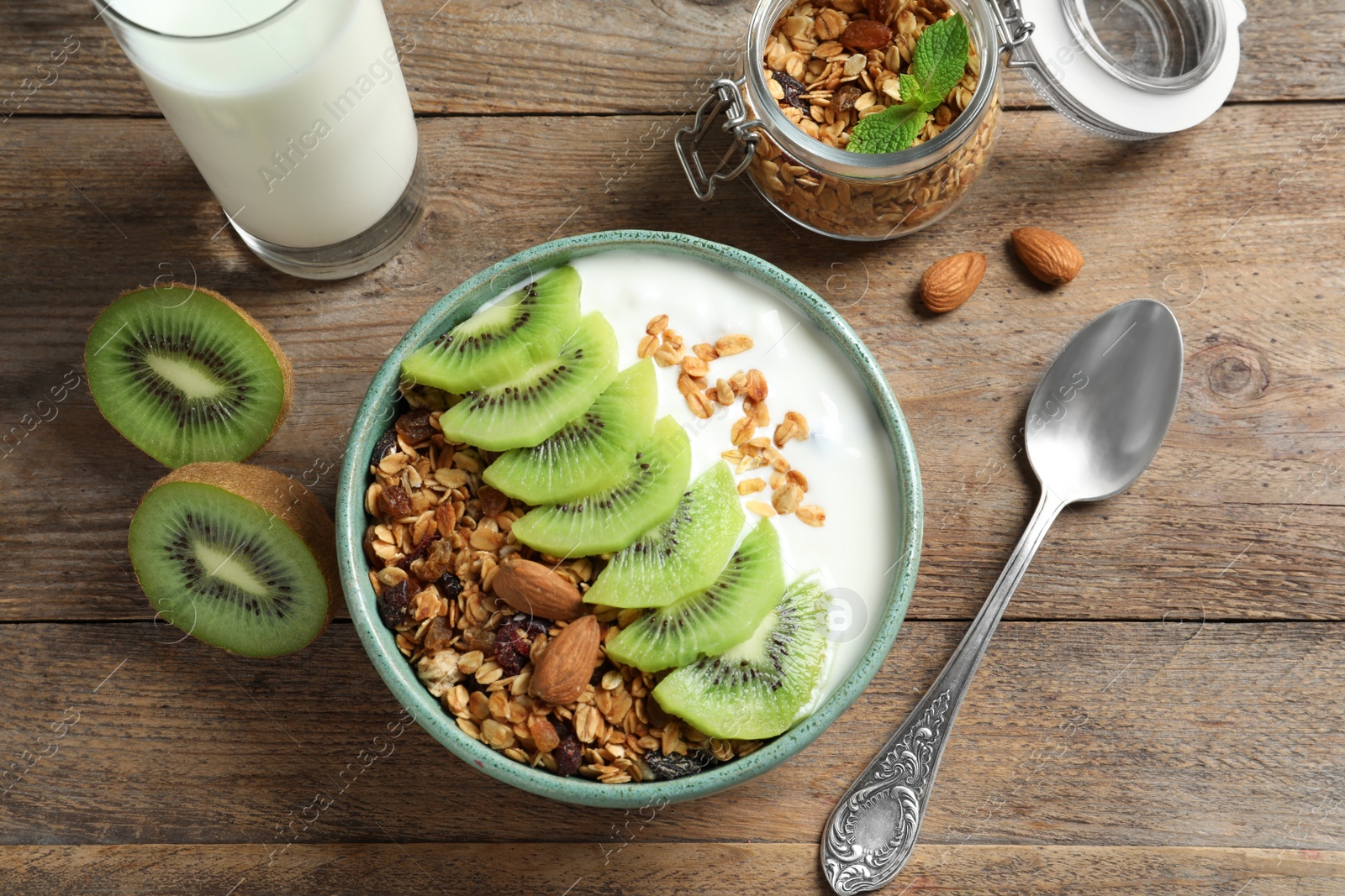 Image of Tasty granola with yogurt and sliced kiwi served for breakfast on wooden table, flat lay