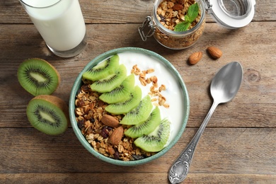 Image of Tasty granola with yogurt and sliced kiwi served for breakfast on wooden table, flat lay