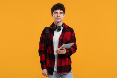 Photo of Portrait of student with backpack, headphones and tablet on orange background