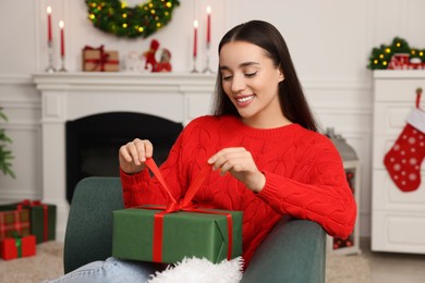 Photo of Happy young woman opening Christmas gift at home