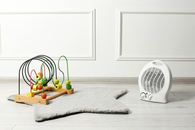 Photo of Modern electric fan heater and colorful toy on rug indoors