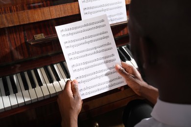 Photo of African-American man with note sheets at piano, closeup. Talented musician