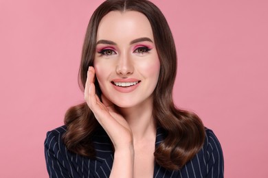 Portrait of beautiful young woman with makeup and gorgeous hair styling on pink background