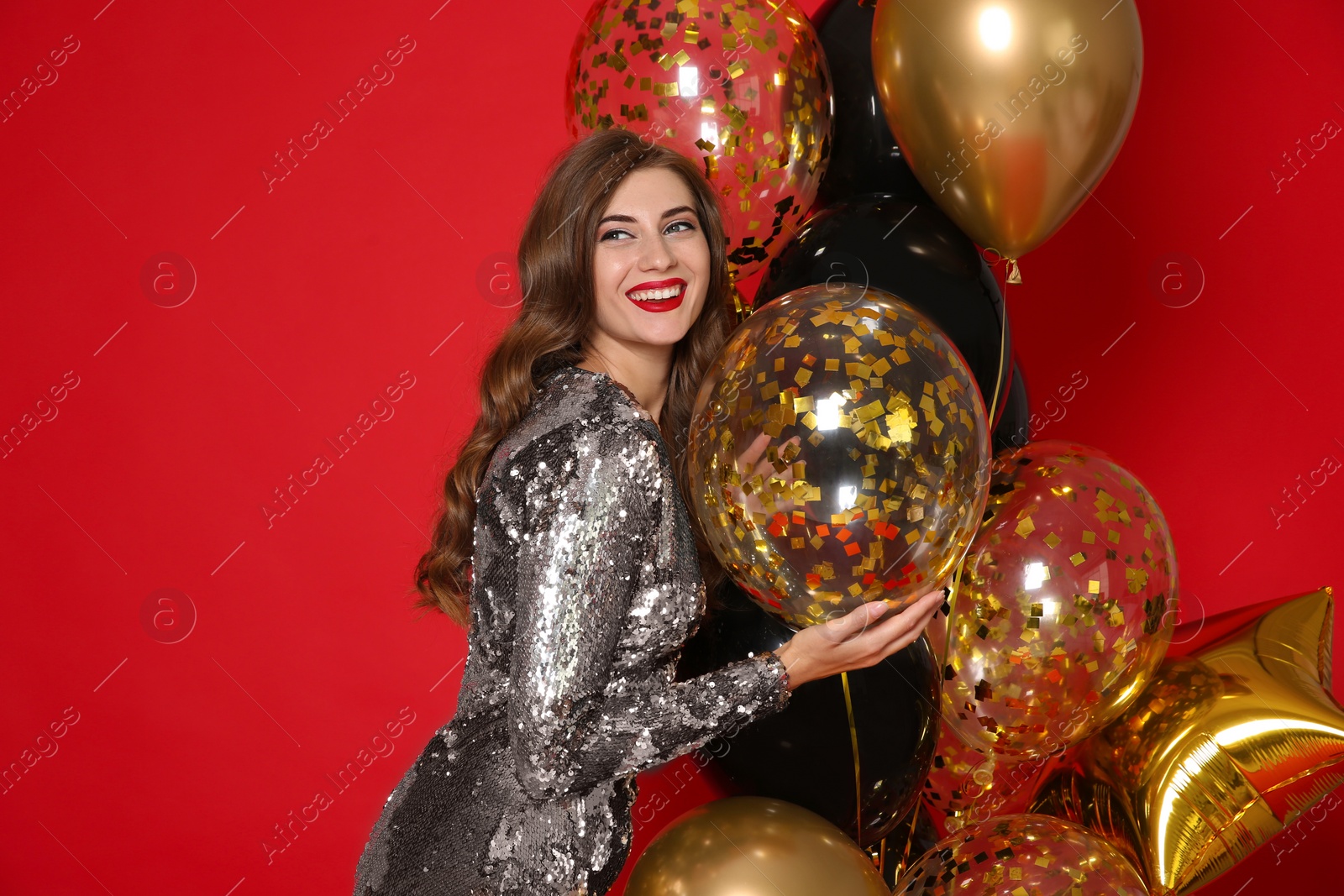 Photo of Happy woman in silver shiny dress with air balloons on red background. Christmas party