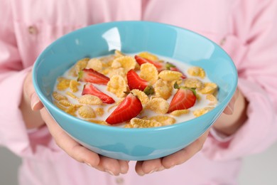 Photo of Woman holding bowl of crispy corn flakes with milk and strawberries, closeup