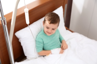 Photo of Little child with intravenous infusion in hospital bed, focus on drip chamber