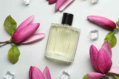 Beautiful pink magnolia flowers, bottle of perfume and ice cubes on light grey background, flat lay