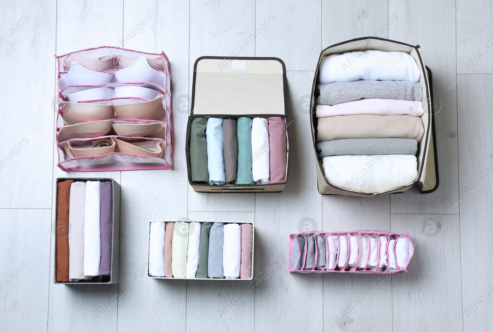 Photo of Different organizers with folded clothes and underwear on white wooden background, flat lay. Vertical storage