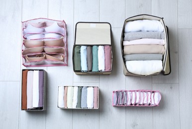 Different organizers with folded clothes and underwear on white wooden background, flat lay. Vertical storage