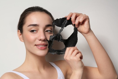 Beautiful young woman removing black mask from her face on white background