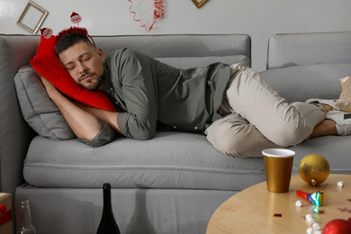 Photo of Man sleeping on sofa in messy room after New Year party