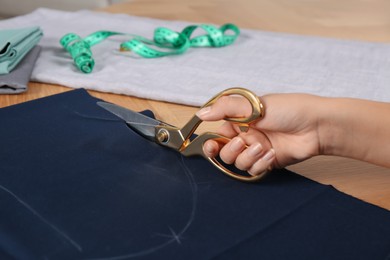 Photo of Woman cutting blue fabric with scissors at wooden table, closeup