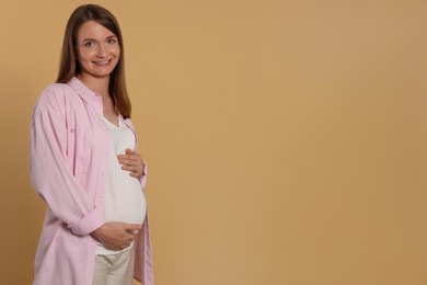 Photo of Happy young pregnant woman on light brown background. Space for text