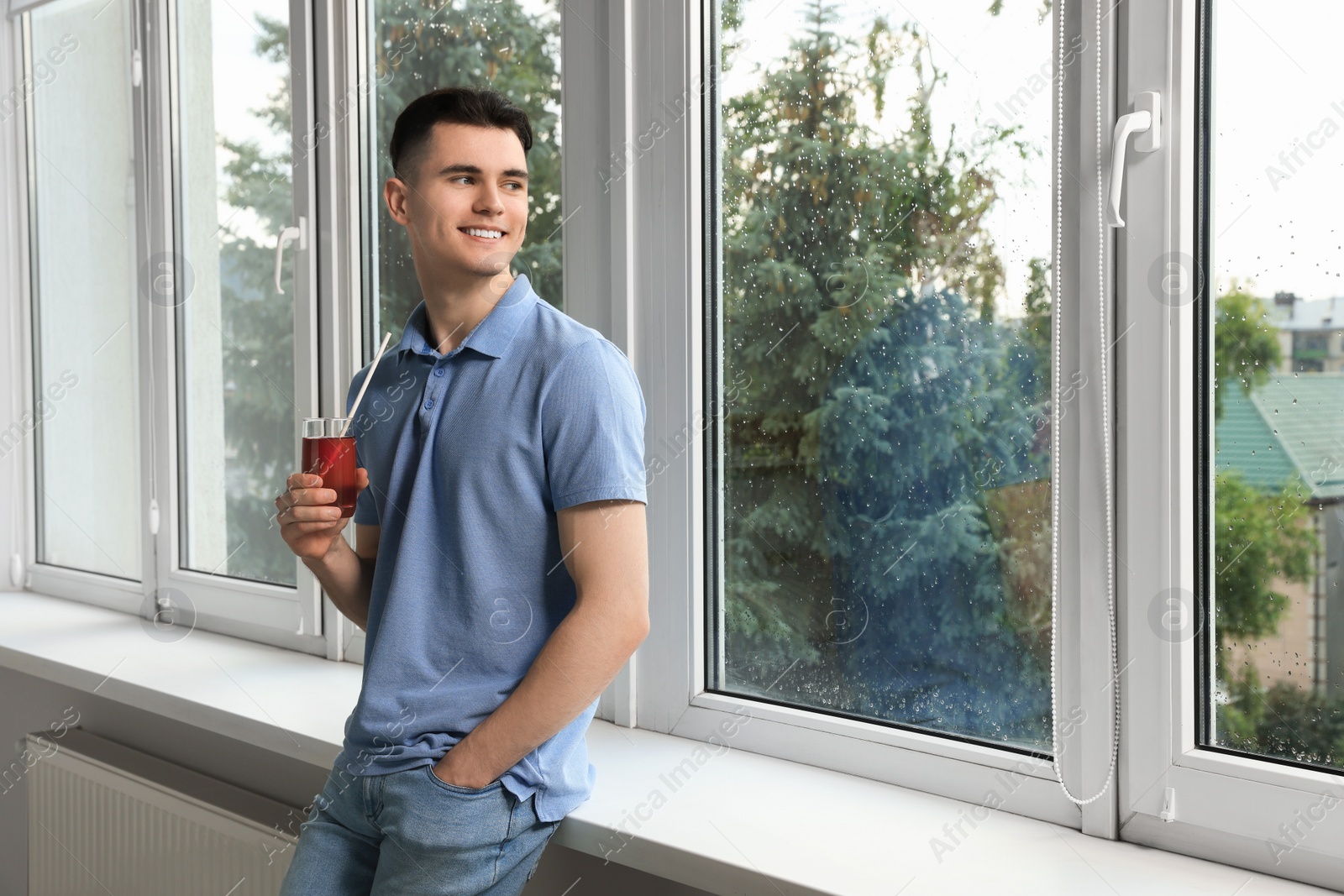 Photo of Handsome young man with glass of juice near window at home